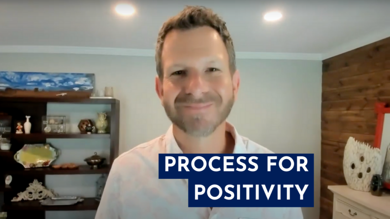 Man in white shirt smiling in front off bookcase with the words Process For Positivity in white on a dark blue background